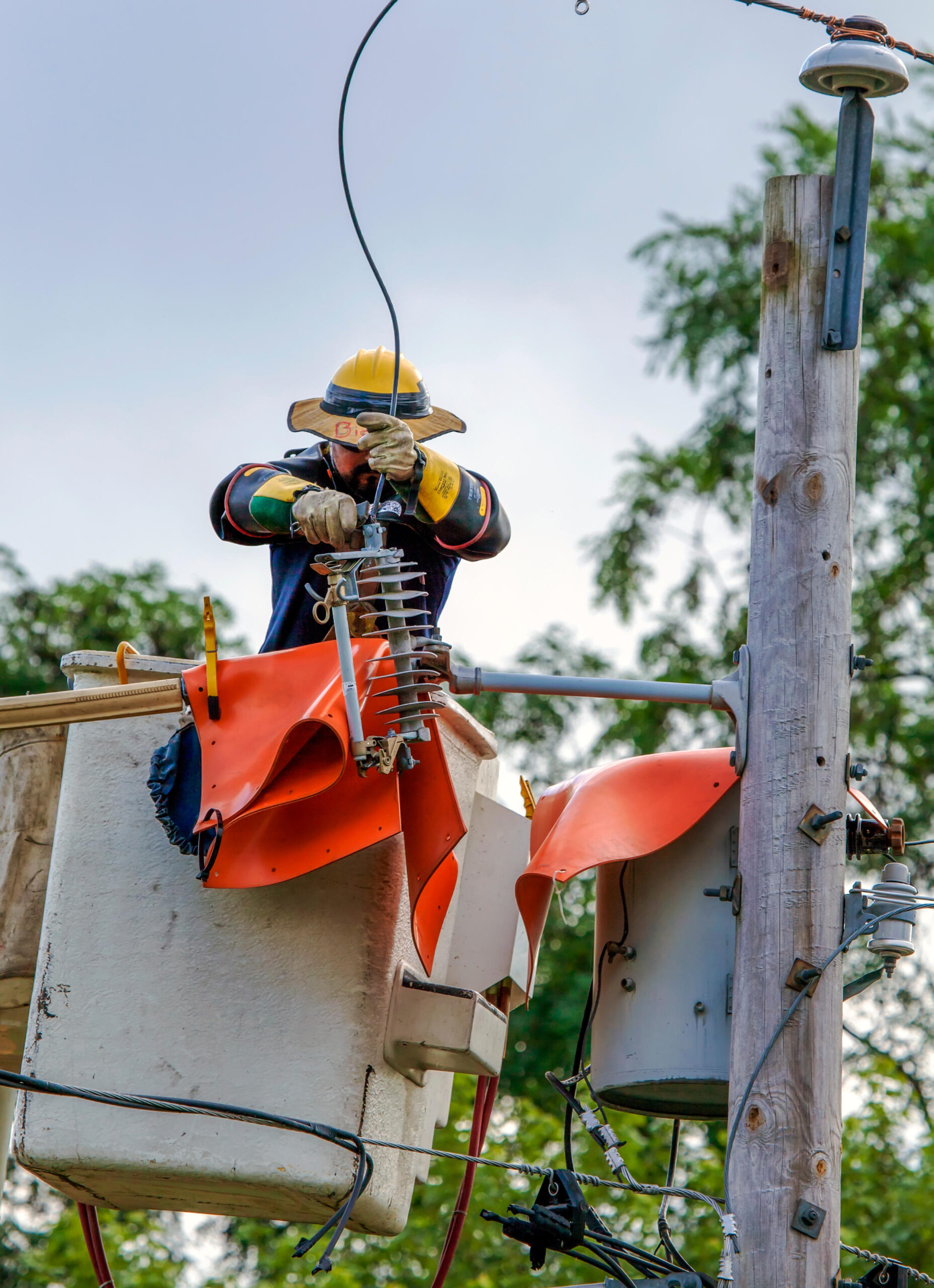 ETG13P A lineman in safety gear connects high voltage power lines using a cherry picker, also called a man lift or boom crane.